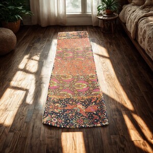 May include: A long, rectangular runner rug featuring a patchwork design of various floral and botanical patterns in vibrant shades of orange, pink, yellow, and dark blue, with visible horizontal stitching throughout the fabric surface.