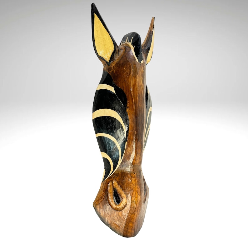 May include: Wooden zebra head sculpture with black and white stripes and yellow accents. The sculpture is carved from wood and painted with black, white, and yellow paint.