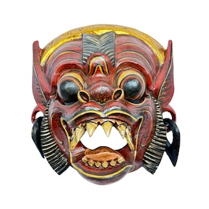 May include: A red, black, and gold wooden mask with a fierce expression. The mask has large, round eyes, a wide mouth with sharp teeth, and intricate details carved into the wood.