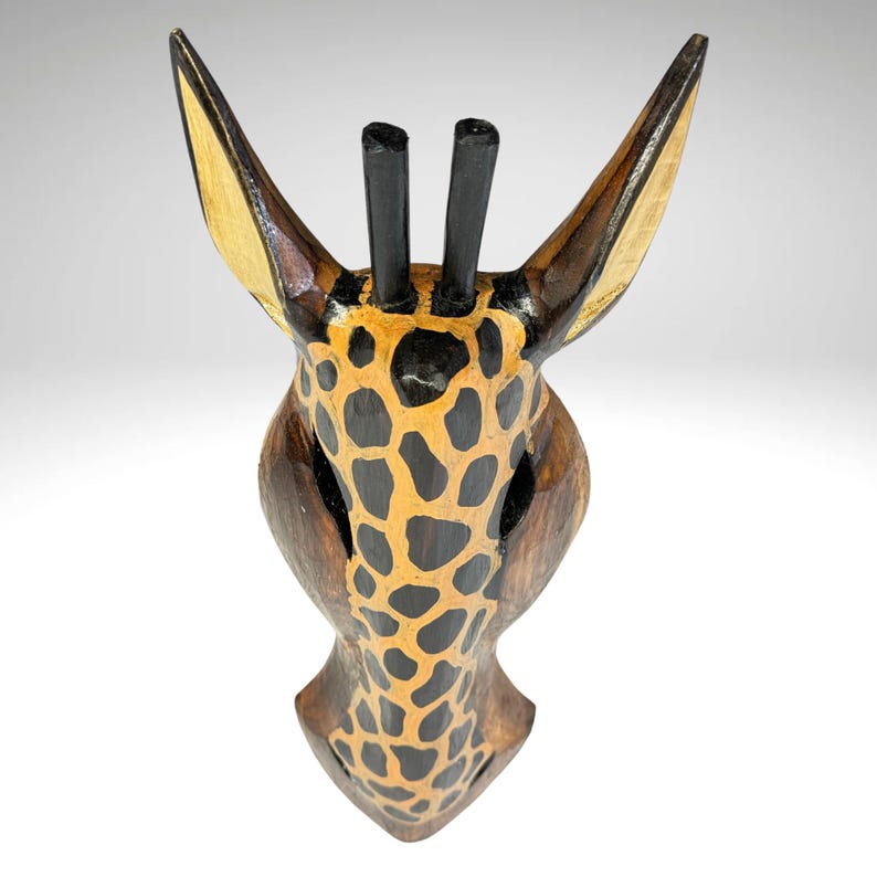 May include: Wooden giraffe head wall decor with a brown, black, and yellow painted giraffe pattern. The giraffe has two black horns on top of its head.