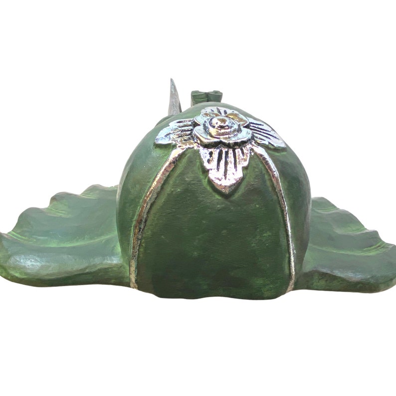 May include: Green ceramic figurine of a reclining Buddha with a silver floral design on the head. The figurine is resting on a lotus leaf.
