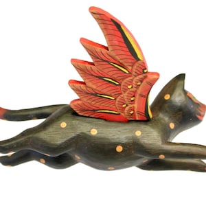 May include: A dark brown wooden cat figurine in a leaping pose with yellow polka dots and large, upright red wings featuring black and yellow feather details. The cat has a long tail and is depicted in a mid-air motion against a white background.