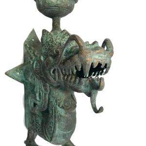 May include: A detailed bronze-colored dragon sculpture with a bowl-shaped top. The dragon has sharp teeth, a long tongue, and intricate details. The sculpture is mounted on a wall and has a weathered appearance.