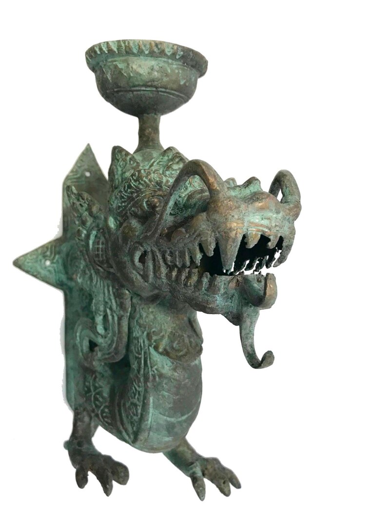 May include: A detailed bronze-colored dragon sculpture with a bowl-shaped top. The dragon has sharp teeth, a long tongue, and intricate details. The sculpture is mounted on a wall and has a weathered appearance.