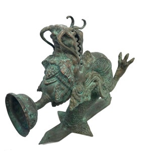 May include: A detailed bronze sculpture of a mythical creature with intricate carvings. The sculpture features a bell-shaped element and a stylized base. The bronze has a weathered, verdigris finish, giving it an antique appearance.
