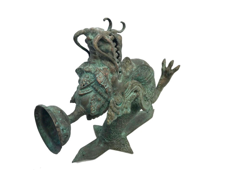 May include: A detailed bronze sculpture of a mythical creature with intricate carvings. The sculpture features a bell-shaped element and a stylized base. The bronze has a weathered, verdigris finish, giving it an antique appearance.