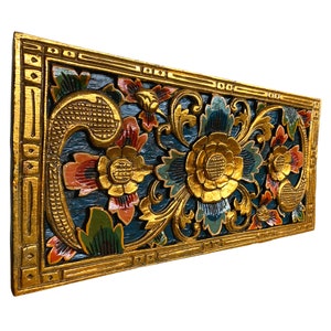May include: A carved wooden wall panel with a floral design. The panel is painted in shades of blue, green, gold, and red. The flowers are intricate and detailed, and the gold paint adds a touch of elegance.