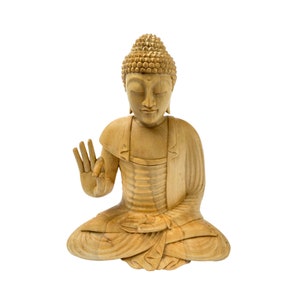 May include: A wooden statue of a seated Buddha with closed eyes and a serene expression. The statue is carved in a light brown color and has a detailed design.