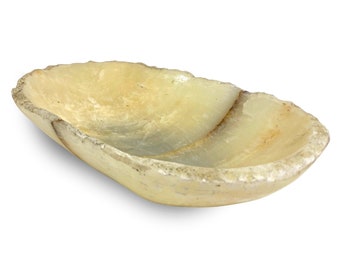 May include: A large, oval-shaped, white alabaster bowl with a rough, textured exterior. The bowl is slightly curved and has a smooth, polished interior.
