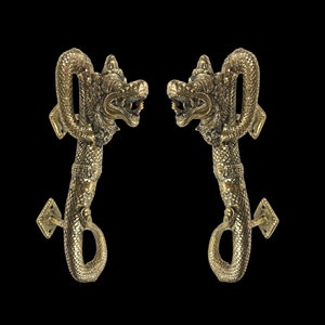 May include: A pair of ornate gold door handles shaped like dragons with their heads facing each other. The handles are detailed with scales and have a decorative design.