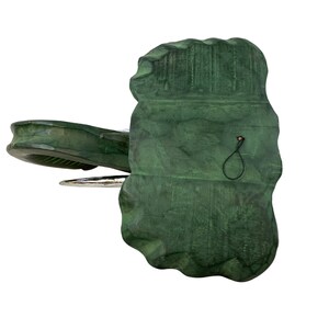 May include: A green ceramic elephant figurine with a silver trunk and a black string hanging from the back. The elephant is standing on a white surface.