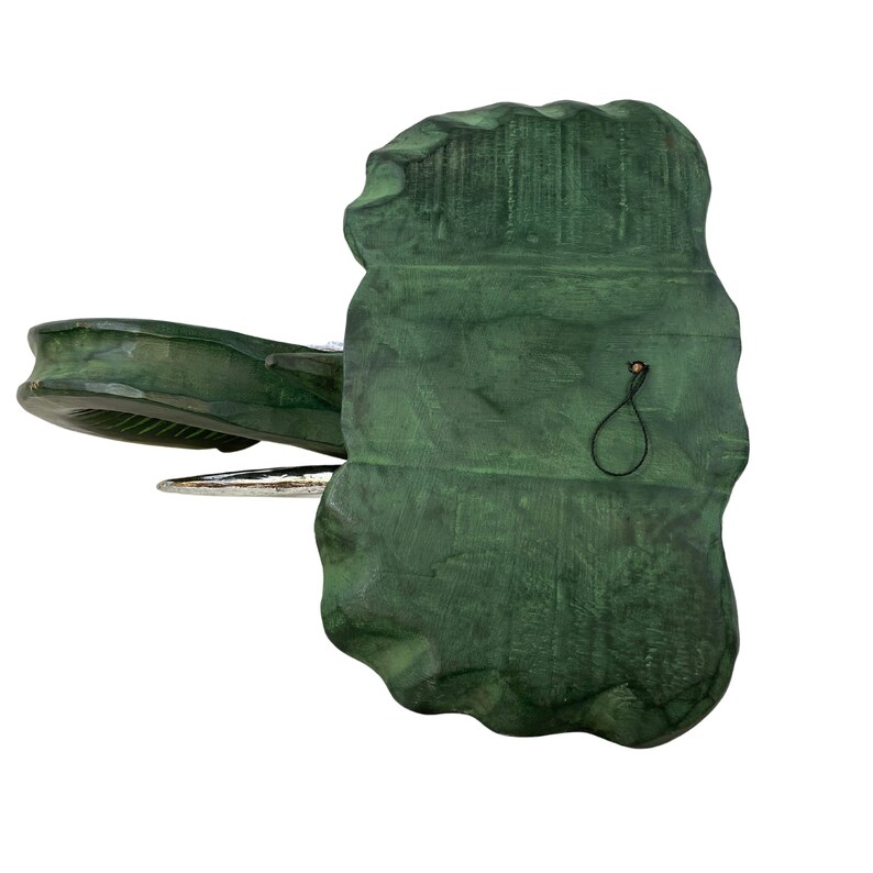 May include: A green ceramic elephant figurine with a silver trunk and a black string hanging from the back. The elephant is standing on a white surface.