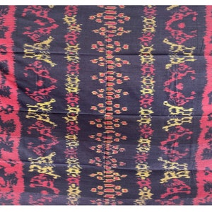 May include: Black fabric with a repeating pattern of red, yellow, and white geometric shapes. The fabric has a woven texture.
