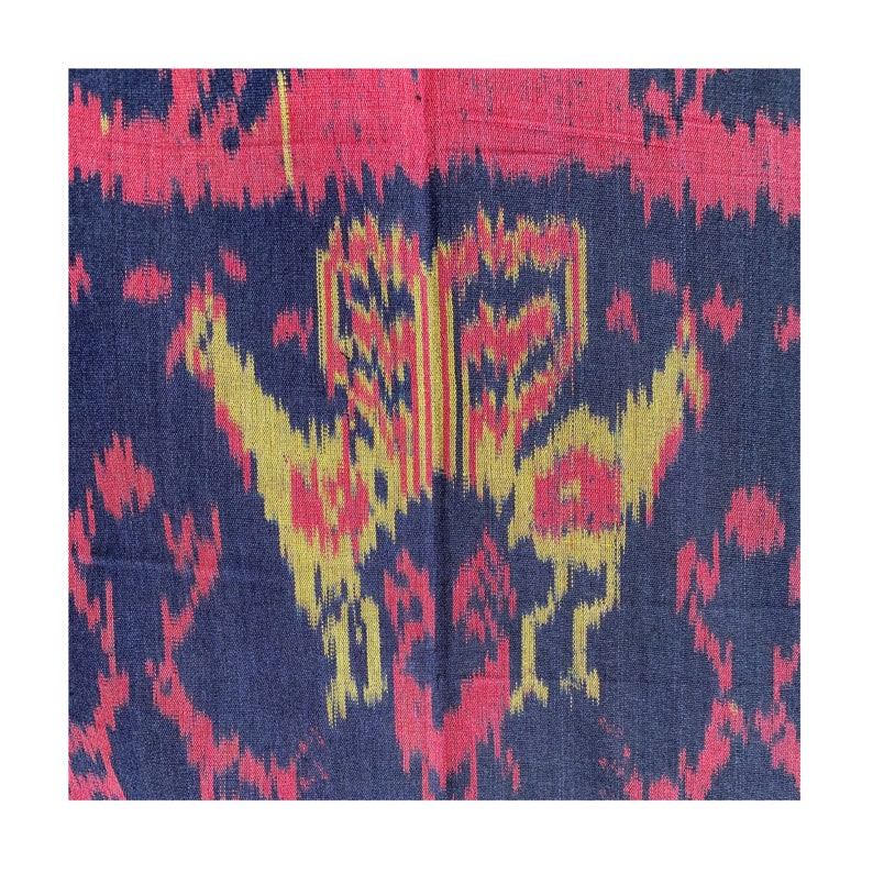 May include: A close-up of a dark blue fabric with a repeating pattern of red, yellow, and gold. The pattern is abstract and resembles a stylized bird.