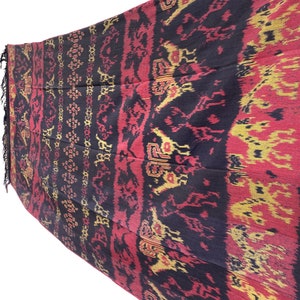 May include: A black, red, and gold woven textile with a repeating pattern of stylized animals. The textile has a fringed edge.