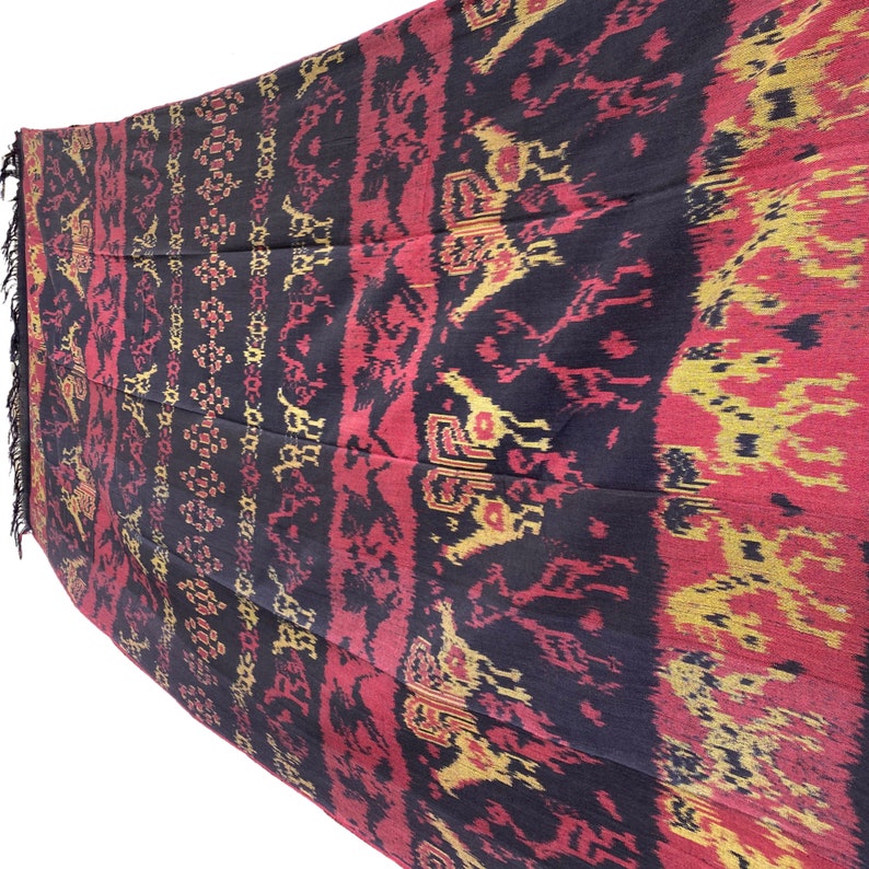 May include: A black, red, and gold woven textile with a repeating pattern of stylized animals. The textile has a fringed edge.