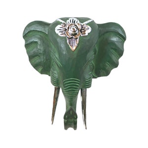 May include: Green wooden elephant head wall decor with a silver floral design on the forehead.