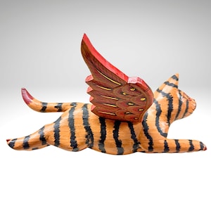 May include: A wooden sculpture of a cat with orange and black stripes, and red wings with gold accents. The cat is in a flying pose, with its paws extended. The sculpture is a decorative item.