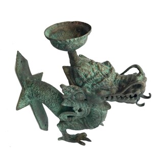 May include: An antique bronze dragon-shaped incense burner. The dragon has a detailed head with open jaws and a small bowl held above its head. The dragon's body is intricately detailed with scales and decorative elements.