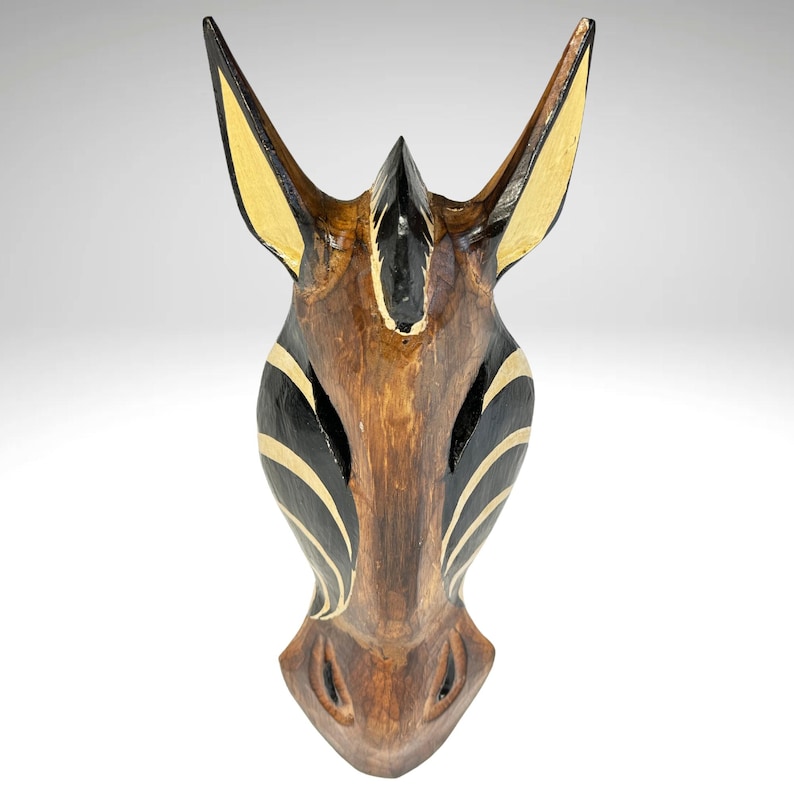 May include: Wooden zebra head wall decor with black and gold stripes. The zebra head is carved from wood and painted with black and gold stripes. It is a unique and decorative piece for any home.