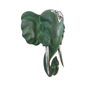 May include: Green wooden elephant head wall decor with silver accents. The elephant has a floral design on its forehead and its tusks are silver.