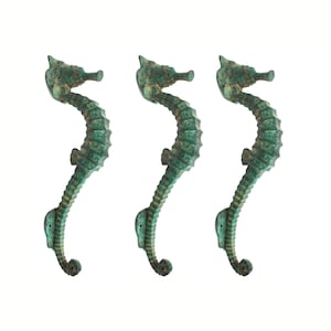 May include: Three green metal seahorse door handles. The handles are in a vertical position and are facing the same direction. The handles are made of a textured metal and have a distressed finish.