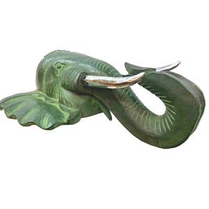 May include: Green wooden elephant head sculpture with silver tusks. The elephant's trunk is curled up and the head is tilted to the side.