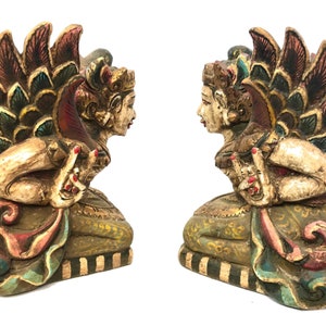 May include: A pair of hand-carved wooden statues of mythical figures with colorful wings and intricate details. The statues are painted in shades of gold, red, green, and blue.
