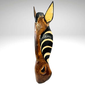 May include: A wooden zebra head wall hanging with black and white stripes and a brown wood finish.