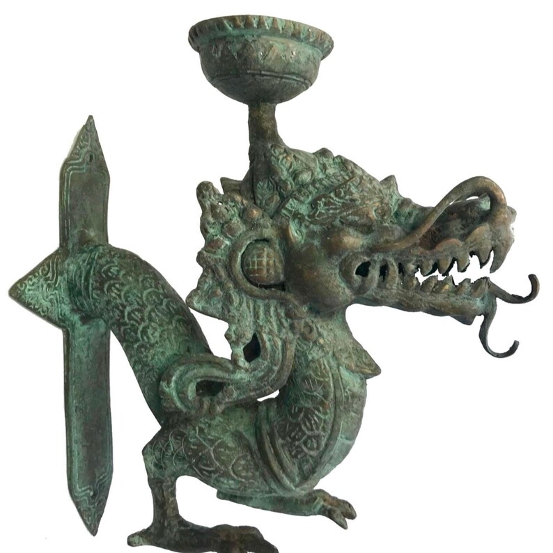 May include: Bronze-colored dragon sculpture with a detailed head, open mouth, and a small bowl-like structure above its head. The dragon has a long, curved tail and intricate scale patterns. The sculpture is on a white background.