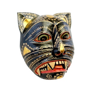 May include: A black wooden mask with gold and red painted details. The mask depicts a stylized animal face with sharp teeth and a fierce expression.