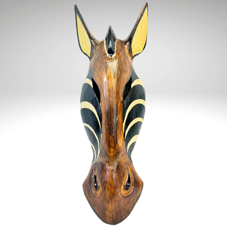 May include: Wooden zebra head mask with black and white stripes and brown wood grain. The mask has a long snout and large, round eyes.