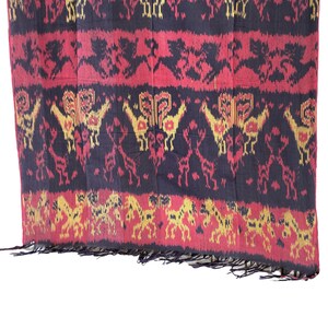 May include: A black, red, and gold woven textile with a repeating pattern of stylized animals. The textile has a fringed edge.