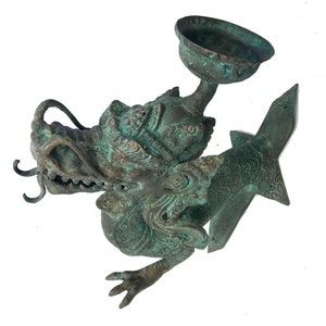 May include: A detailed bronze sculpture of a dragon with a bowl-shaped element. The dragon has intricate details, a textured surface, and a green patina. The sculpture is on a white background.