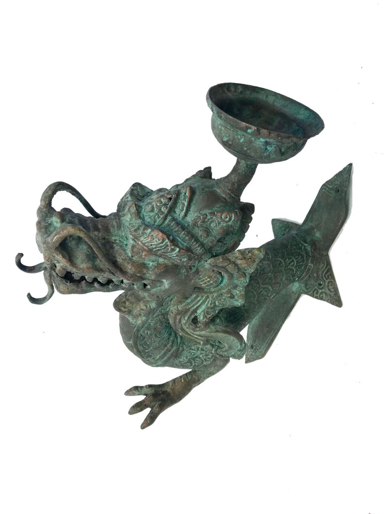 May include: A detailed bronze sculpture of a dragon with a bowl-shaped element. The dragon has intricate details, a textured surface, and a green patina. The sculpture is on a white background.