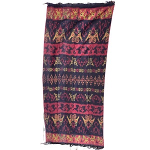 May include: A black, red, and gold woven textile with a geometric pattern. The textile has a fringed edge.