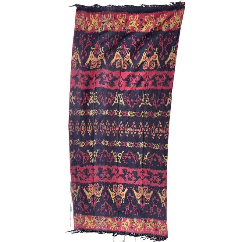 May include: A black, red, and gold woven textile with a geometric pattern. The textile has a fringed edge.