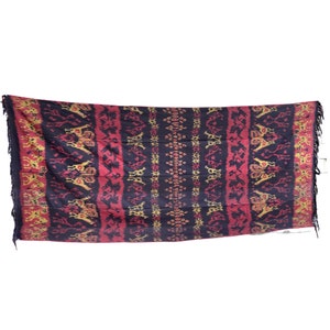 May include: A black, red, and gold woven textile with a geometric pattern. The textile has fringe on all four sides.
