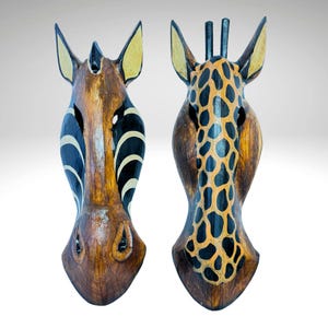May include: Two wooden animal masks, one of a zebra and one of a giraffe. The zebra mask is brown with black and white stripes, and the giraffe mask is brown with orange and black spots.