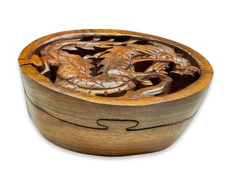 May include: A wooden puzzle box with a carved dragon design. The box is made of dark brown wood and has a hinged lid. The dragon is intricately carved and has a detailed design.
