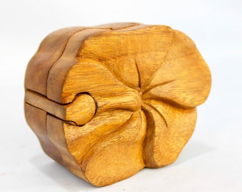 May include: A wooden puzzle box carved in the shape of a flower. The box is made of light brown wood and has a detailed design.