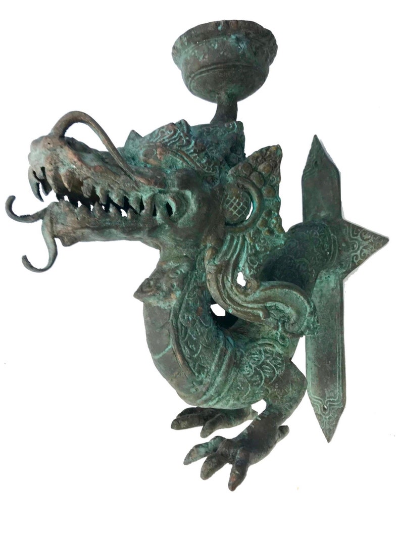 May include: A detailed bronze dragon sculpture with a verdigris finish. The dragon features intricate scales, sharp teeth, and a small cup-like structure on top. The sculpture has a decorative, ornate design.