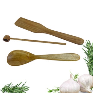 May include: A set of three wooden kitchen utensils: a spoon, a spatula, and a small spoon with a rounded handle. The utensils are made of light brown wood and are arranged on a white background.