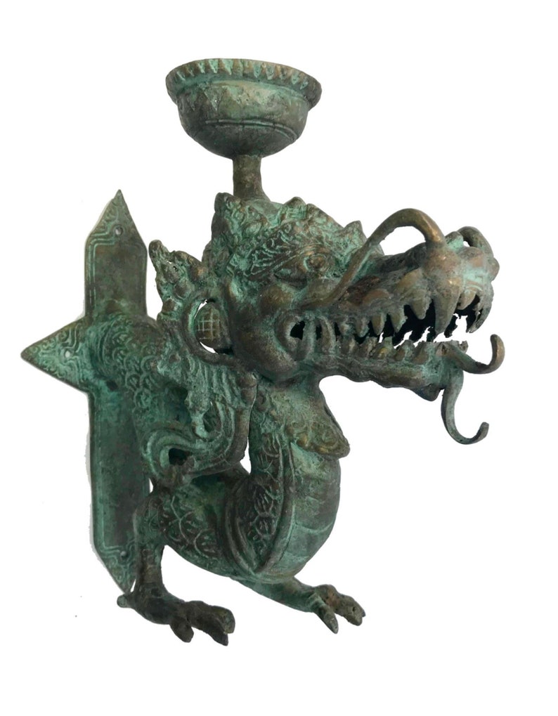 May include: A bronze-colored dragon-shaped wall sconce. The dragon has detailed scales, a fierce expression, and a small bowl at the top. The sconce is designed to hold a candle or small light source, adding a touch of fantasy to any space.