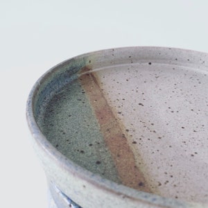 Può includere: Un piatto in ceramica con una glassa marrone chiaro, blu e verde. Il piatto ha una finitura macchiata e un bordo leggermente rialzato.