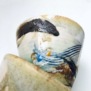 May include: A set of two ceramic bowls with a white glaze and abstract blue, brown, and gold designs. The bowls are stacked on top of each other.