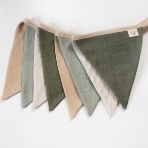 May include: A fabric bunting in shades of beige, green, and white. The triangular flags are attached to a beige ribbon. The bunting is suitable for home decoration and measures approximately 150 cm in length.