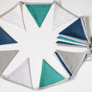 K&ouml;nnte beinhalten: Eine dekorative Wimpelkette mit dreieckigen Flaggen in verschiedenen Farben und Mustern. Die Flaggen umfassen einfarbiges T&uuml;rkis, Marineblau, Grau, Wei&szlig; mit grauen Punkten und Wei&szlig; mit grauen Streifen. Die Flaggen sind mit einem grauen Band verbunden.