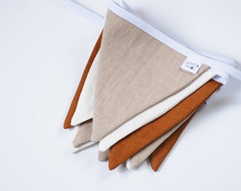 May include: A folded linen banner with a white trim and a brown label that says "Handmade". The banner is made of three different colors: beige, white, and orange.