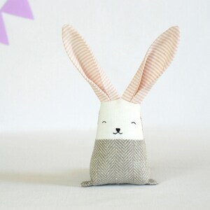 May include: A plush gray and white bunny toy with pink striped ears. The bunny has a simple embroidered face with black eyes and a nose.